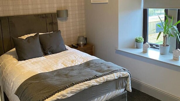 Una camera da letto con un letto, un comodino, una finestra con persiane e una piccola pianta in vaso sul davanzale.