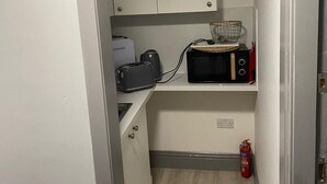 Una piccola cucina accessoriata con mobili bianchi, un tostapane, un forno a microonde e un estintore rosso.