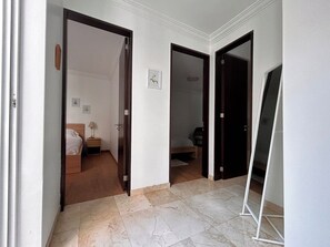 Un couloir donnant accès à deux chambres, chacune équipée d’un lit et d’une table de chevet.