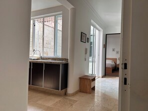 Une cuisine moderne dotée d’un îlot central intégré, un coin repas avec une banquette et une chambre à coucher comprenant un lit et une table de chevet.