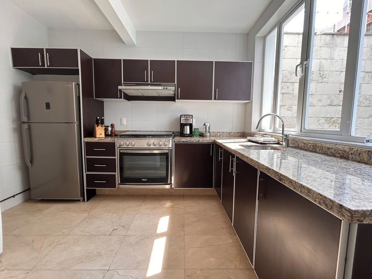A modern kitchen with stainless steel appliances, dark cabinetry, and a large window providing natural light.
