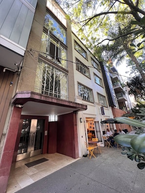 Un immeuble à plusieurs étages doté d’une entrée couverte, d’un espace extérieur aménagé pour s’asseoir et de balcons apparents.