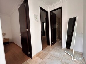 A hallway with a wooden floor, white walls, and a mirror leaning against the wall.
