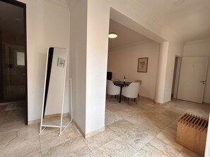 Un hall d’entrée spacieux comprenant un coin repas avec une table et des chaises, un présentoir pour tableau blanc et une poubelle en bois.