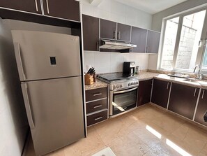 Une cuisine moderne dotée d’appareils électroménagers en acier inoxydable, de meubles de rangement aux couleurs sombres et d’une grande fenêtre qui laisse entrer la lumière naturelle.