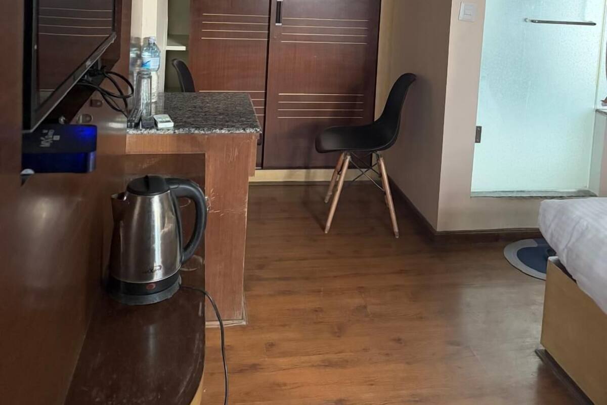 A compact hotel room with a wooden desk, a television, a wardrobe, a bed, and a small kitchenette area.