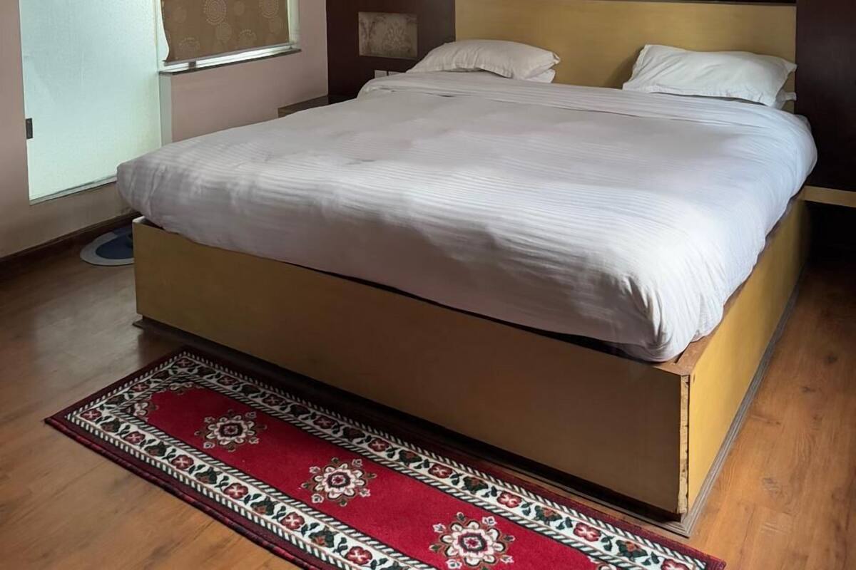 A bedroom with a bed, a window, a door, and a patterned rug.