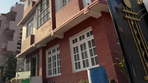 A multi-story building with a red and white facade, large windows, and a gated entrance. - Cosy Stay & Dine (Kathmandu)