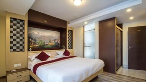 A modern hotel room with a large bed, a checkered wall decoration, a painting of a landscape, and a dark wooden door. - Cosy Stay & Dine (Kathmandu)