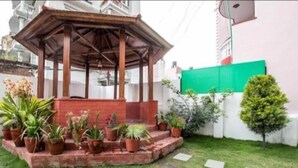 A gazebo with a brick base and wooden beams, surrounded by potted plants and a small tree. - Cosy Stay & Dine (Kathmandu)