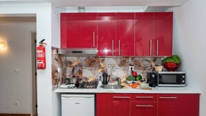 Une cuisine de taille réduite avec des meubles rouges, un lave-vaisselle blanc, un four à micro-ondes et un extincteur.