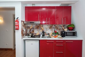 Une cuisine compacte avec des meubles rouges, une hotte de cuisinière en acier inoxydable, un four à micro-ondes et un lave-vaisselle.