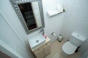 Casa de banho com lavatório, espelho, sanita e um armário com artigos de higiene pessoal.