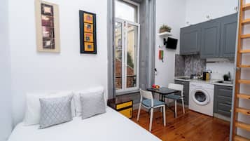 Um espaço compacto com cama, mesa pequena, cadeira, máquina de lavar e cozinha.