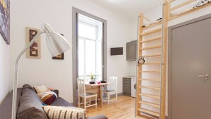 A compact living space with a sofa, a dining table, chairs, a TV, a wardrobe, and a wooden ladder. - Studio Apartment Located Central Lisbon (Lisbon)