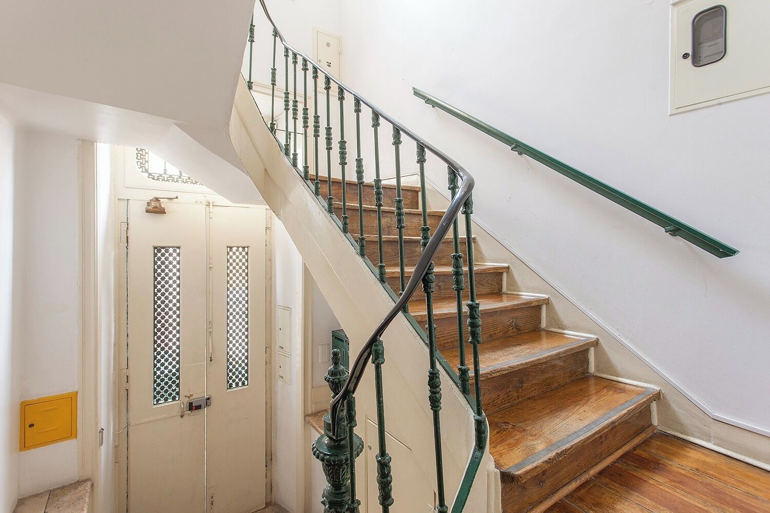 Escada com balaústres verdes e degraus de madeira que levam a um patamar.