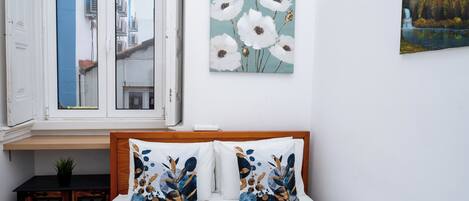 A bedroom with a bed, pillows, a window, and a wall with a painting.