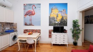 A kitchen with a washing machine, a dining table with chairs, a TV on a stand, and a red sofa. - 2 Bedroom Apartment Located Heart of Lisbon City (Lisbon)