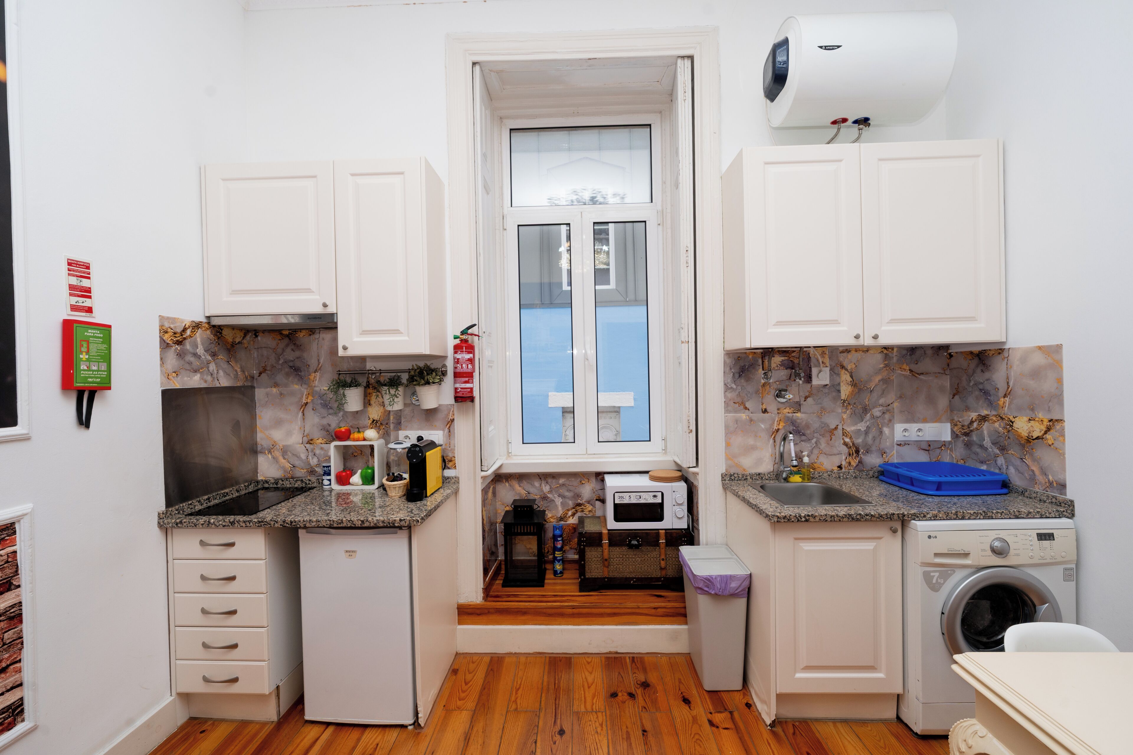 A compact kitchen with white cabinets, a built-in microwave, a washing machine, and a small window.