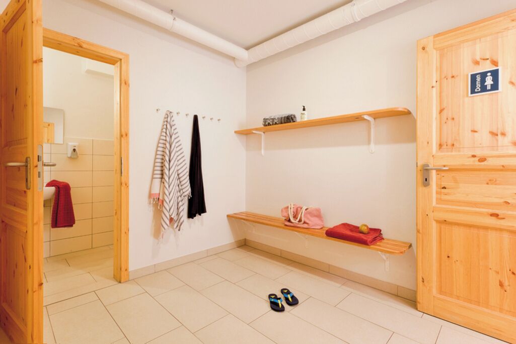 Une salle de bain épurée et minimaliste, avec un banc en bois, des étagères et un espace douche.