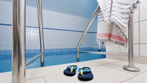 A swimming pool area with a tiled floor, a metal pool ladder, and a pair of flip-flops on the edge.