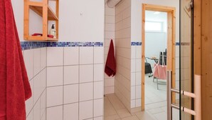 A bathroom with white tiles, a wooden shelf, and a red towel.