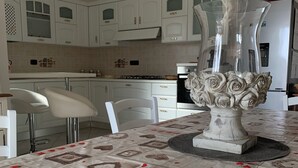 A modern kitchen with white cabinetry, a central island with a decorative vase, and a patterned tablecloth. - Don Michele Apartments (Gizzeria)