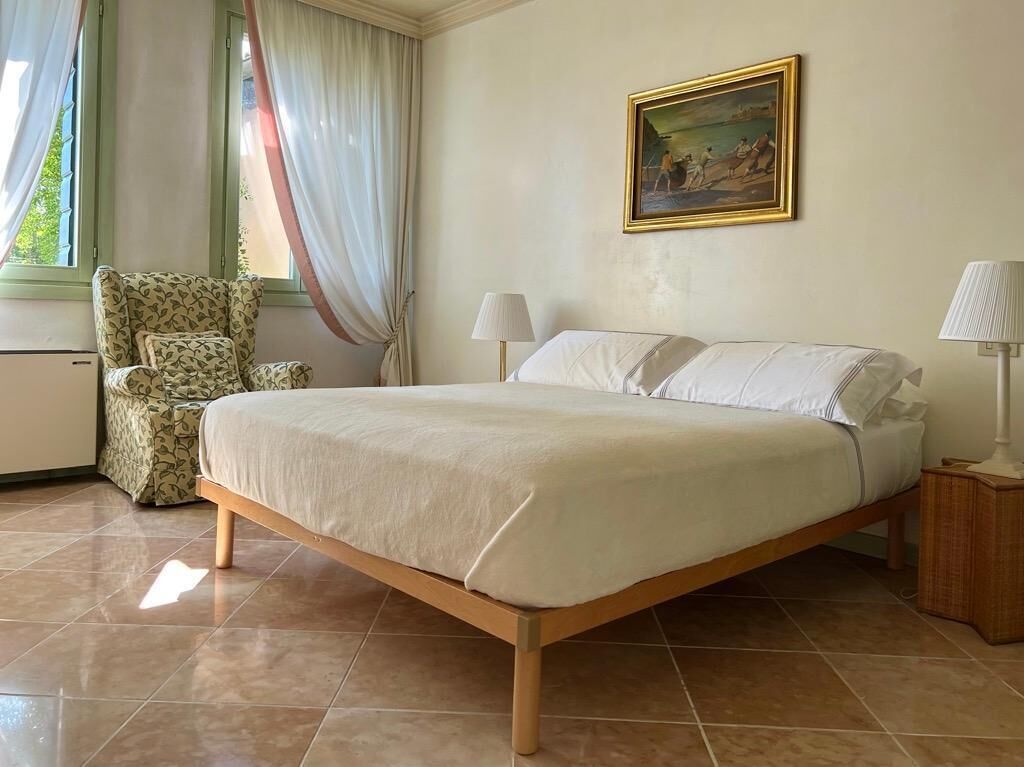 A bedroom with a bed, a chair, a lamp, and a painting on the wall.