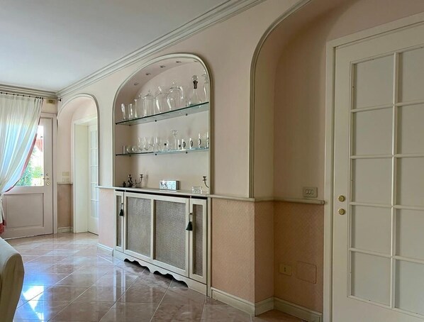 A room with a white cabinet with glass shelves, a door with a grid pattern, and a tiled floor.