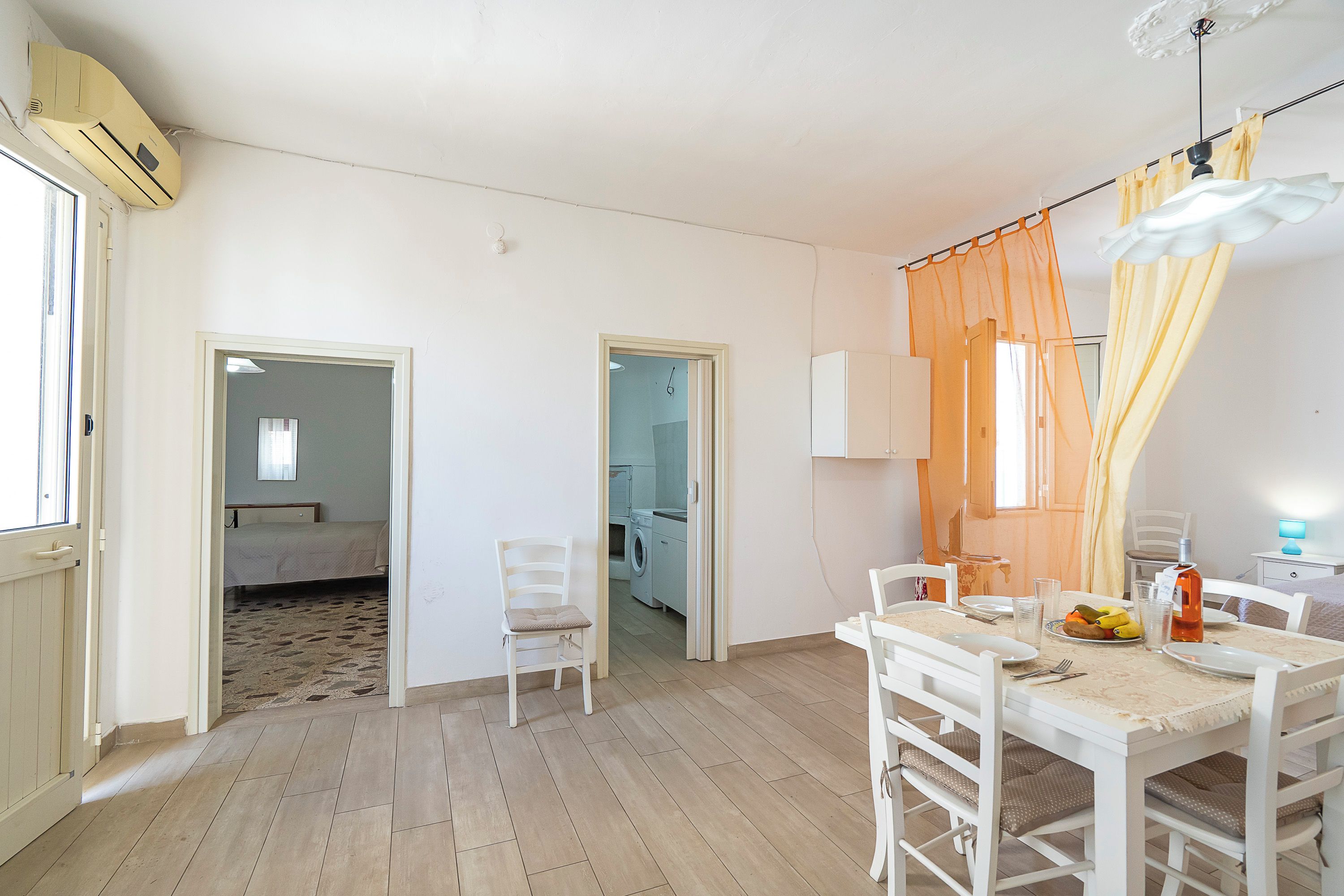 A room with a dining table set for two, a chair, a bed, and a washing machine in the background.