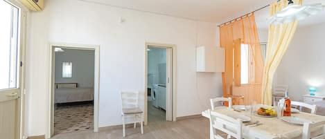 A room with a dining table set for two, a chair, a bed, and a washing machine in the background.
