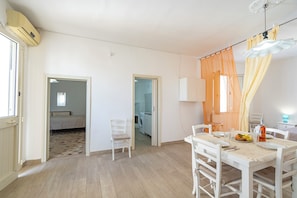 Una habitación con una mesa de comedor lista para dos personas, una silla, una cama y una lavadora al fondo.