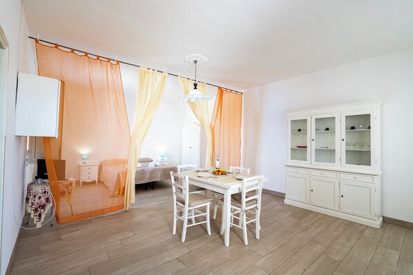 A room with a dining table, chairs, a cabinet, and a bed with curtains.