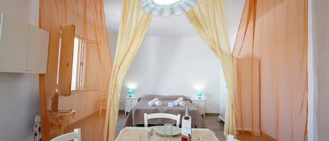 Habitación de hotel con cama, una mesa de comedor con sillas, un frutero y una botella de agua.