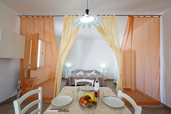 Habitación de hotel con cama, una mesa de comedor con sillas, un frutero y una botella de agua.