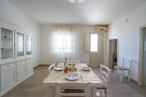 A dining area with a table set for four, white chairs, a cabinet with glass doors, and a window with sheer curtains.