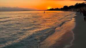 En strand med solnedgang, roligt hav og et par personer der går langs kysten.