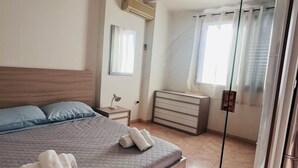 Et moderne soveværelse med en stor seng, et natbord med lampe, en kommode og en skydedør til et badeværelse.