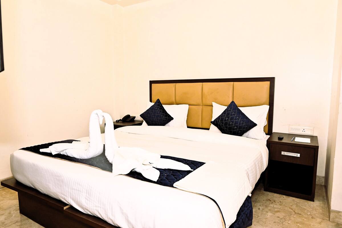 A neatly made bed with a white and dark blue color scheme, a wooden nightstand with a phone and a small table, and a wall socket.
