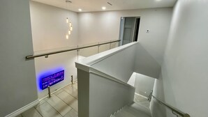 A modern staircase with a glass railing, recessed lighting, and a wall-mounted display.