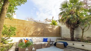 Eine Terrasse mit einem Korbsessel, einem kleinen Tisch und einer Laterne.