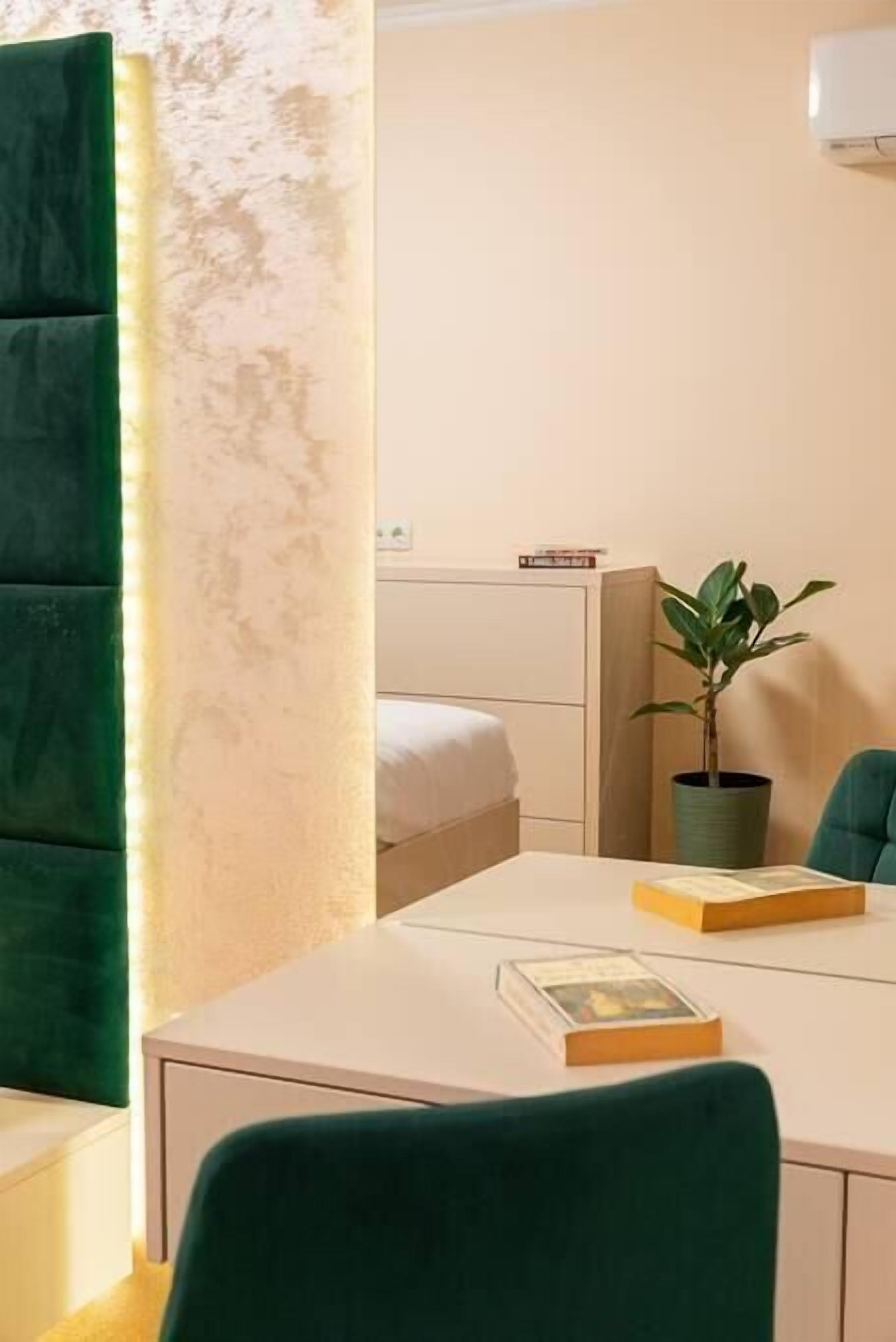 A hotel room with a bed, a desk with a chair, a potted plant, and a bedside table with a book.