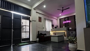 A modern living room with a black tiled floor, ceiling fans, a sofa, a coffee table, and a reception desk with a neon sign. - Sunita Residency (Gurugram)