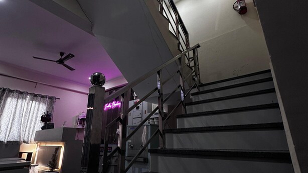 A modern staircase with metal railings, a ceiling fan, and a neon sign. - Sunita Residency (Gurugram)