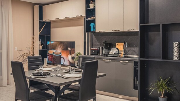 Een moderne keuken met een eethoek, met een grote flatscreen-tv, een koffiezetapparaat en inbouwplanken.