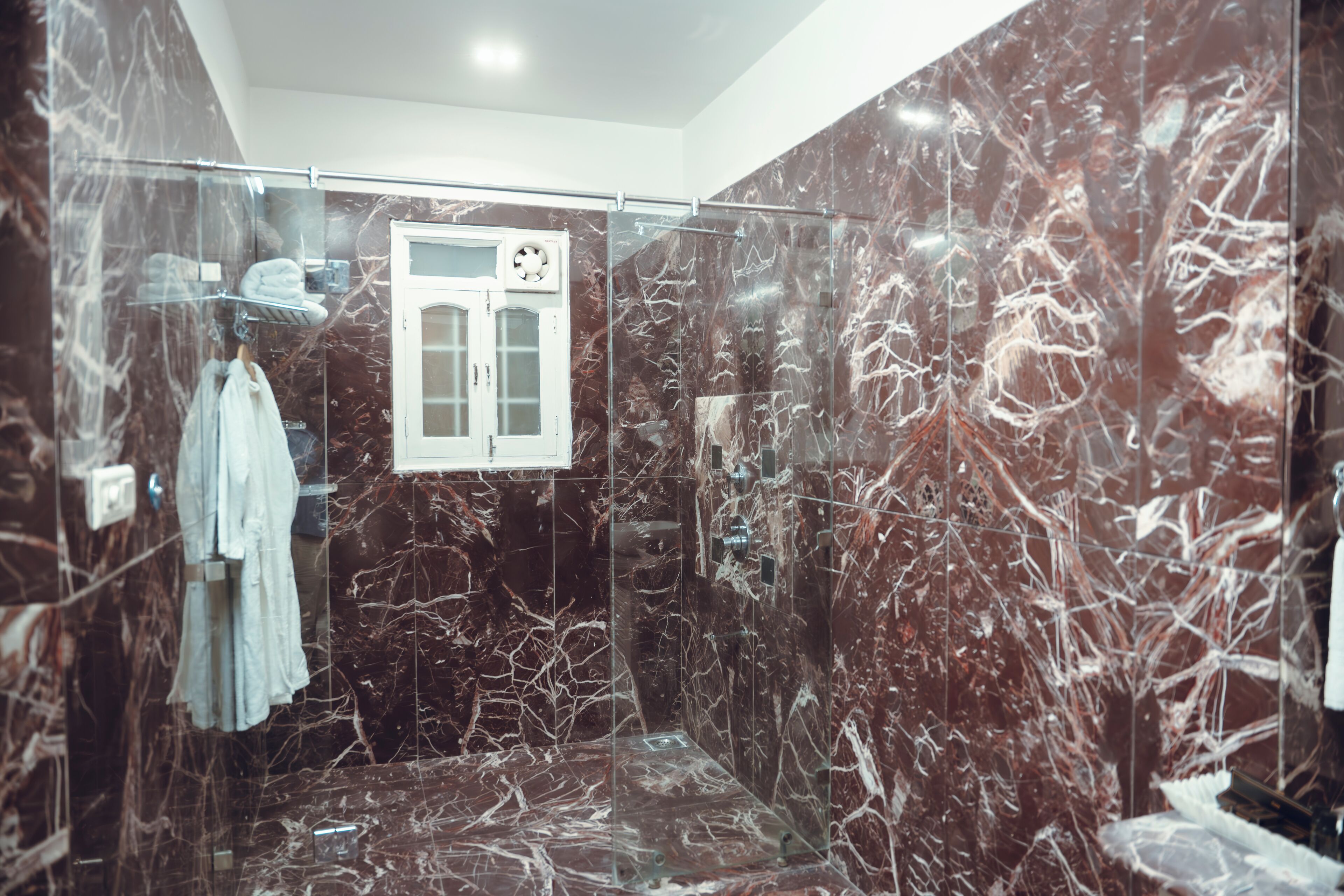 A modern bathroom with a glass-enclosed shower, marble walls, and a towel rack with towels.