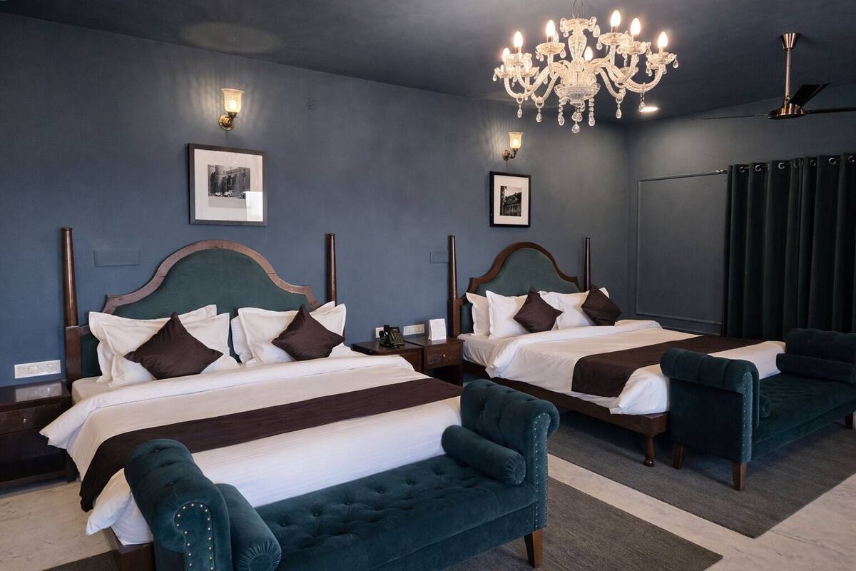 Habitación de hotel con dos camas, un candelabro y un ventanal grande con cortinas.