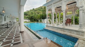 A pool area with a checkered floor, white columns, and a view of a lush hillside. - Victoria Mansion - A Signature Collection by HST Hotels (Udaipur)