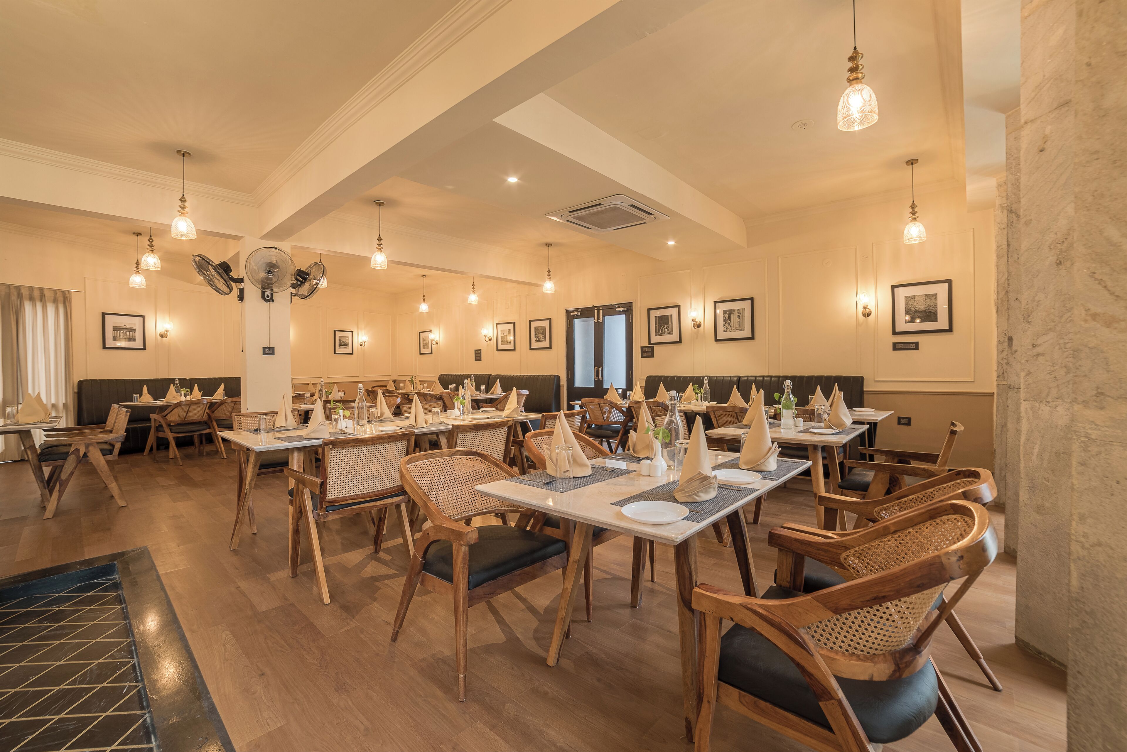 A restaurant with wooden tables and chairs, hanging light fixtures, and framed pictures on the walls.