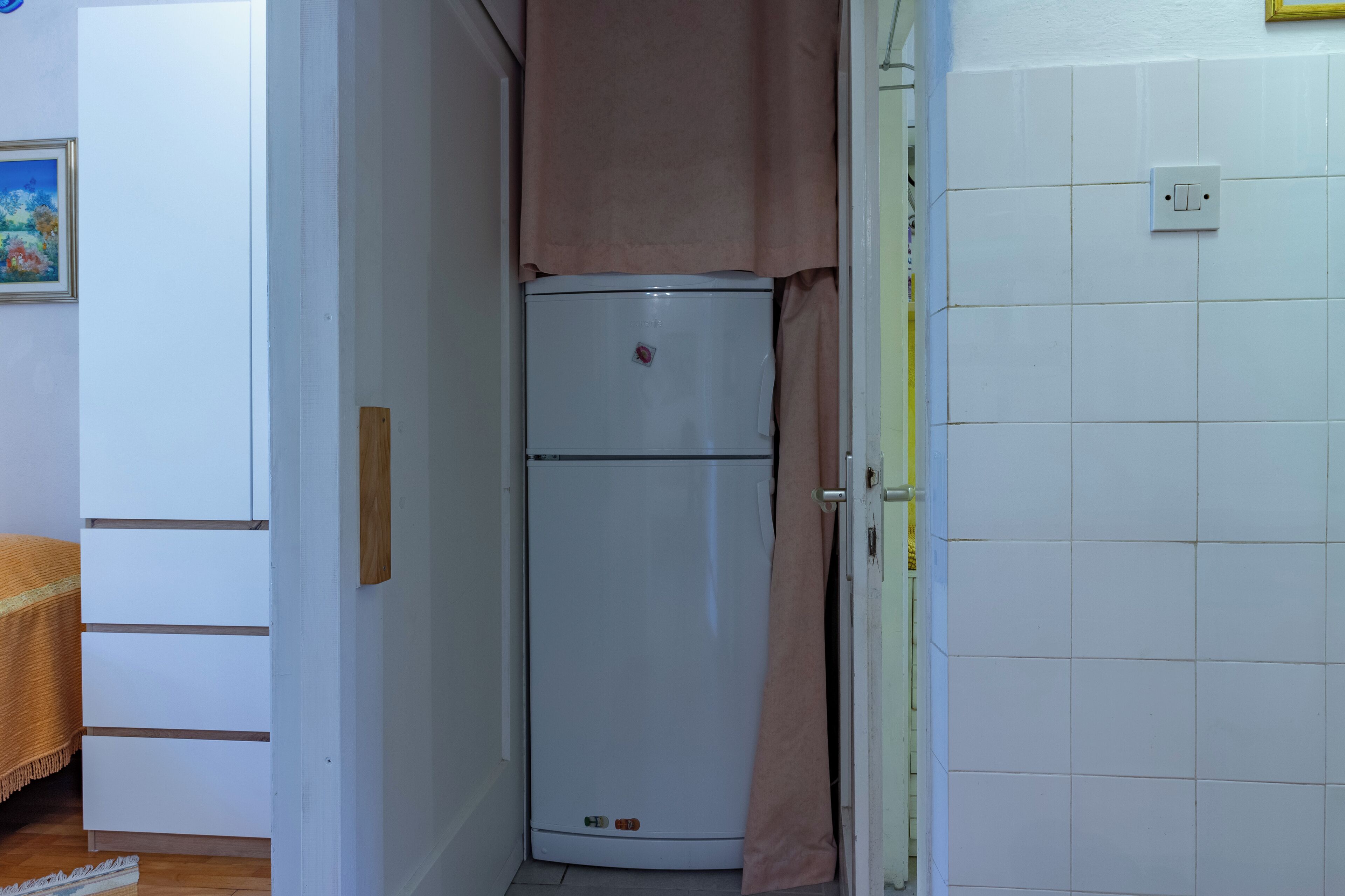 Een kleine keuken met een witte koelkast, een houten kastje en een betegelde spatwand.